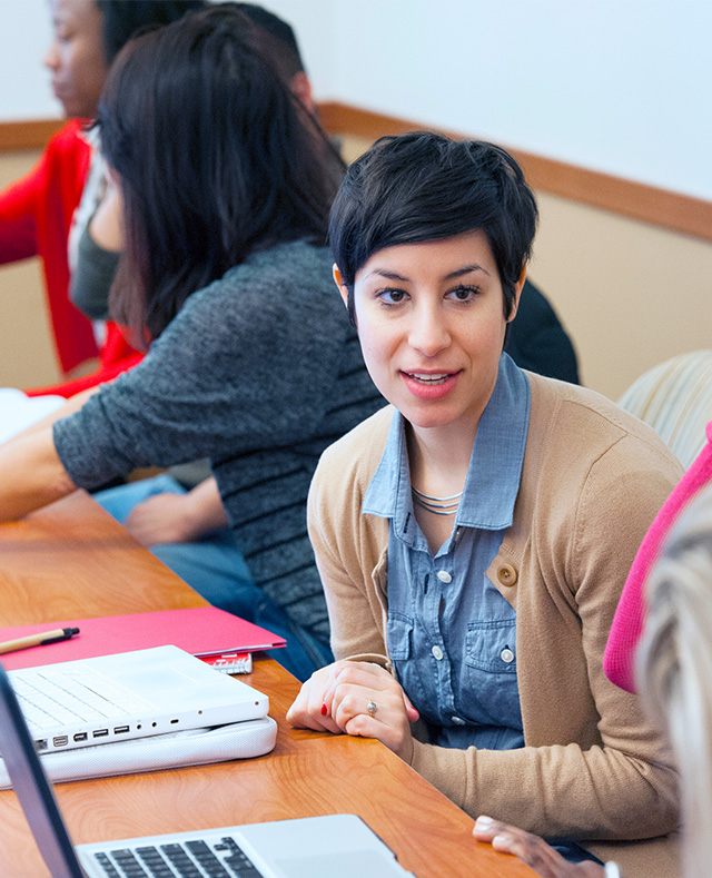 Student at a desk talking with other s.